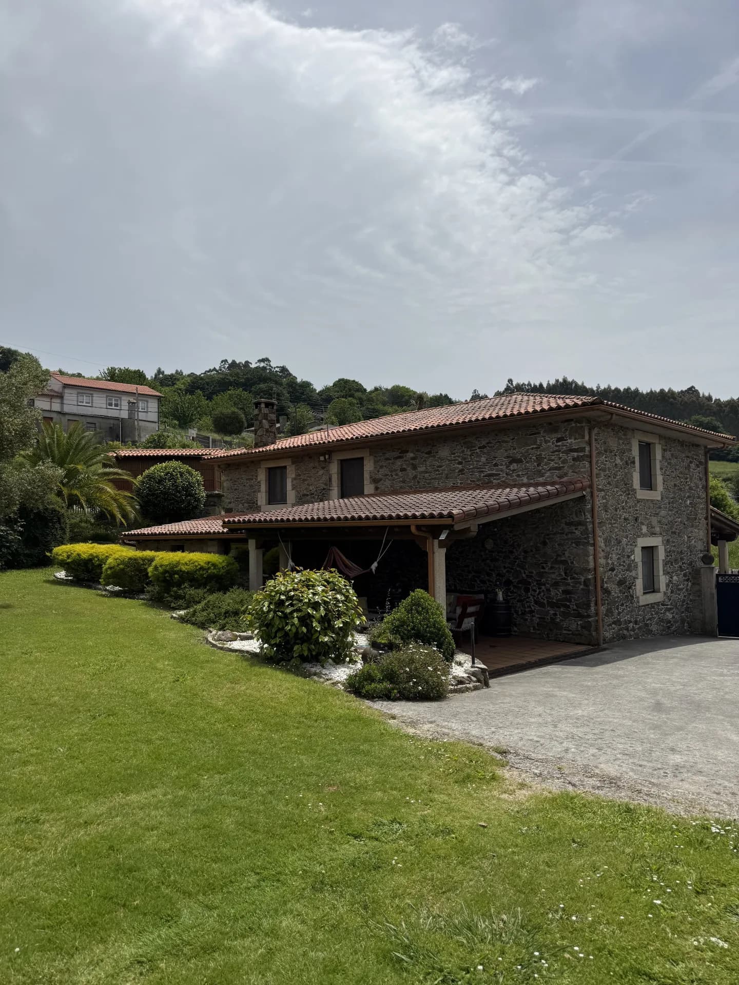 Fachada de piedra de O Lar do Carpinteiro con porche de madera, jardín y bosque en Oza dos Ríos